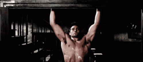 a shirtless man is flexing his muscles on a bar in a dark room .