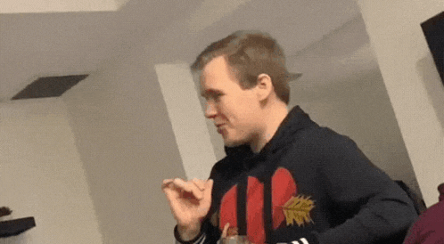 a man in a black hoodie with a red heart on it is sitting at a table eating something .