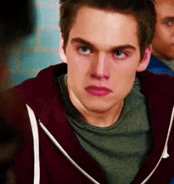 a young man wearing a maroon hoodie and a green shirt is making a funny face .