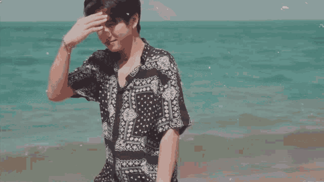 a man wearing a bandana shirt stands on the beach
