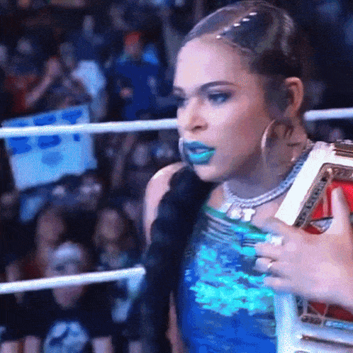 a woman with blue lipstick is holding a championship belt in a ring .