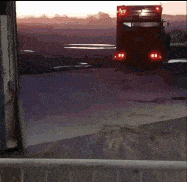 a red truck is driving down a road at sunset with a sunset in the background