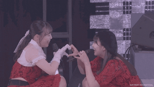 two women are making a heart shape with their hands in front of a microphone and the word international is on the bottom