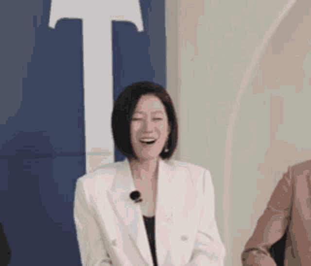 a woman in a white jacket is laughing in front of a blue and white wall .