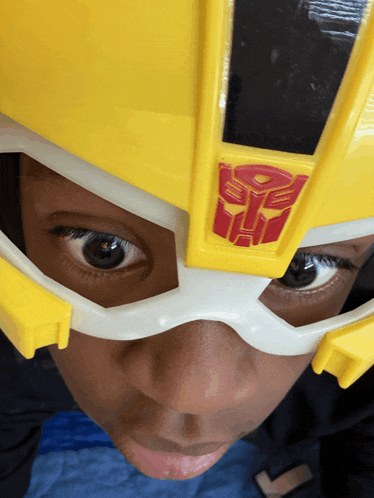 a child wearing a yellow and white helmet with a transformer logo on it
