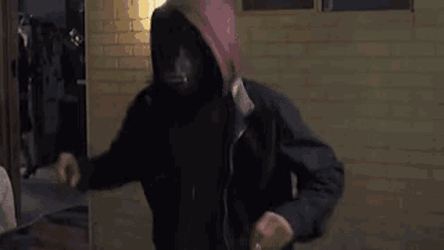 a man in a hooded jacket is holding a knife in front of a brick wall .
