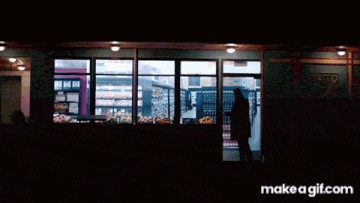a man in a black coat is standing in a grocery store looking at shelves and a make a gif.com button