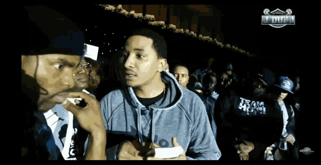 a man in a gray hoodie stands in front of a crowd with the word duke on the bottom