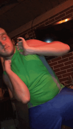 a man in a green shirt and blue shorts is standing in front of a brick wall with his arms outstretched