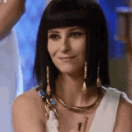 a woman in a costume is smiling and wearing a necklace and earrings .
