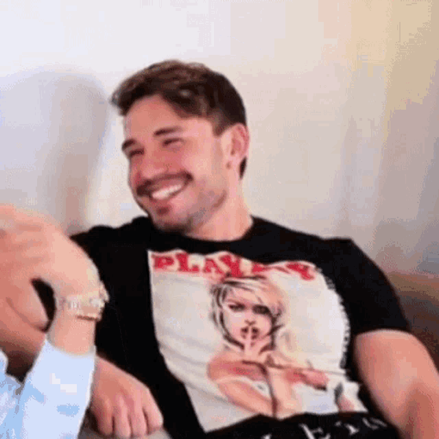 a man wearing a black playboy t-shirt is sitting on a couch .