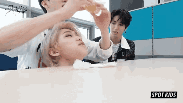 a group of young boys are sitting at a table and one of them is drinking from a bottle .
