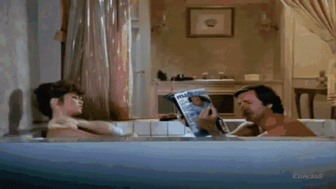 a man and a woman are sitting in a bathtub . the man is reading a magazine .