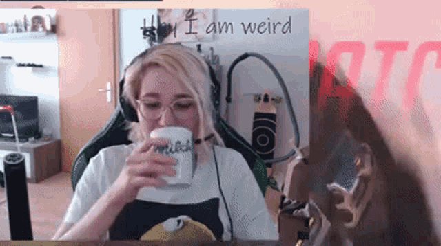 a woman wearing headphones and glasses is drinking from a cup with the words i am weird written on it