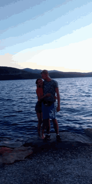 a man and a woman standing on a rock near a body of water