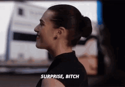 a woman in a black dress is standing in front of a computer screen and saying surprise bitch .