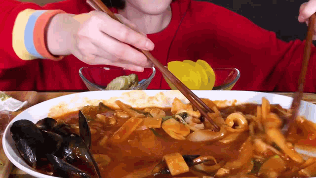 a person in a red sweater is eating a plate of food with chopsticks