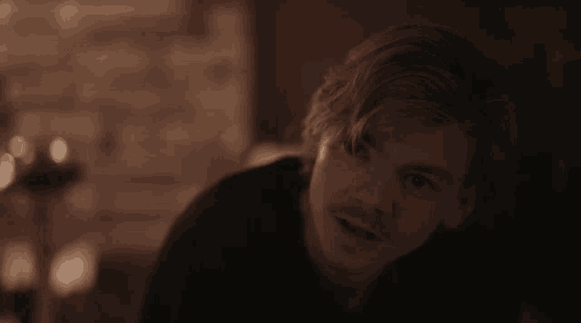 a close up of a man 's face in a dark room with a brick wall in the background