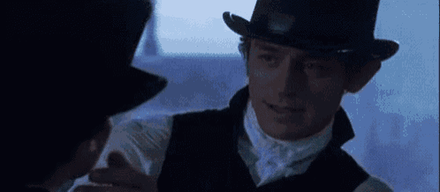 a man wearing a top hat is talking to another man in a dark room .