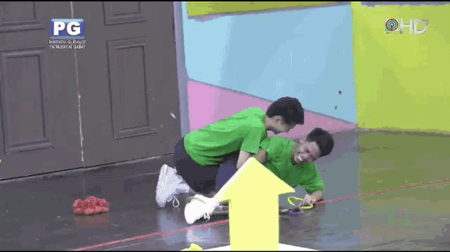 two men in green shirts are playing a game with a yellow arrow .
