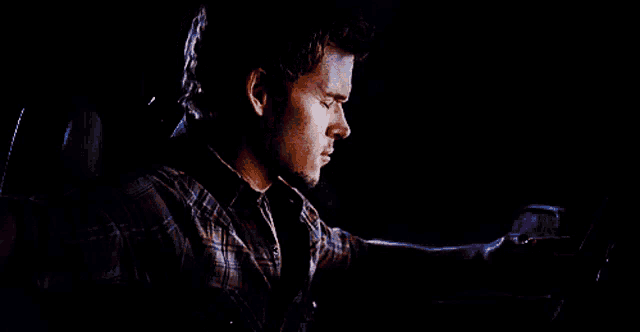 a man in a plaid shirt is driving a car