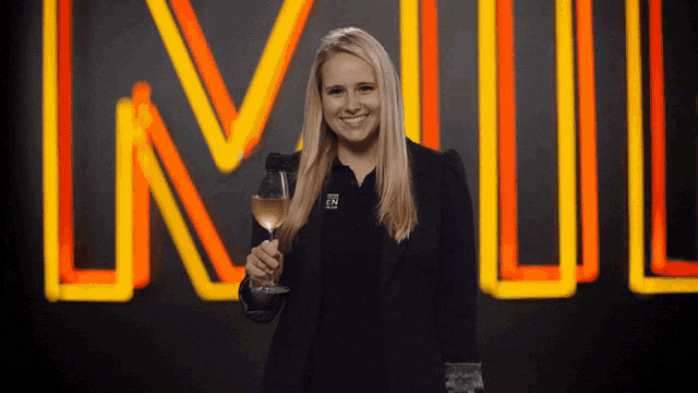 a woman holding a glass of wine in front of a neon sign that says lnw