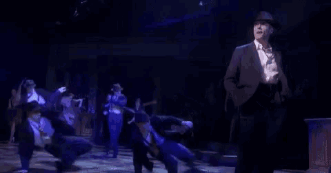 a man in a suit and hat is dancing on stage with a group of people .
