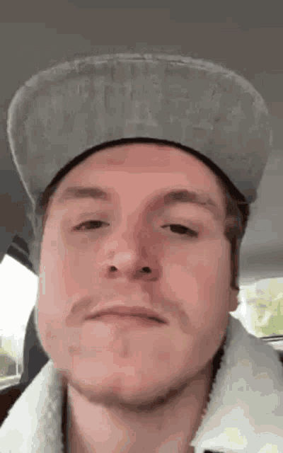 a man wearing a hat and a white jacket is making a funny face .
