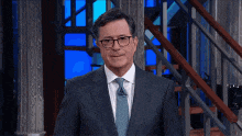a man in a suit and tie is standing in front of a staircase .