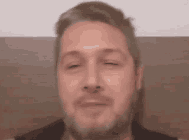 a man with a beard is making a face with his eyes closed .