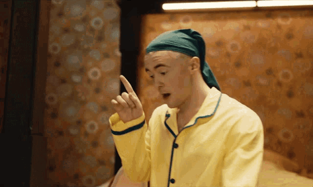 a man wearing a yellow pajama top and a green turban is pointing up