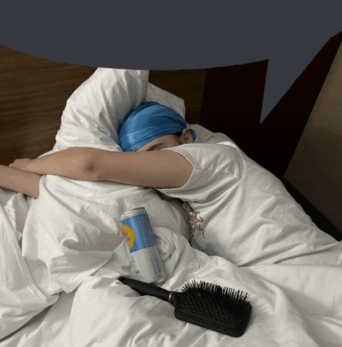 a person is sleeping on a bed with a can of beer and a hairbrush