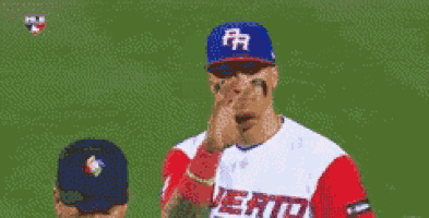 a baseball player wearing a blue hat with the letter r on it is covering his face .