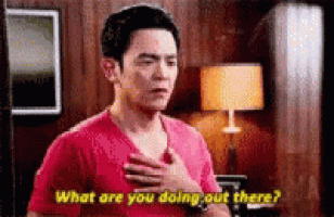 a man in a red shirt is standing in a living room with his hand on his chest and asking what are you doing out there .