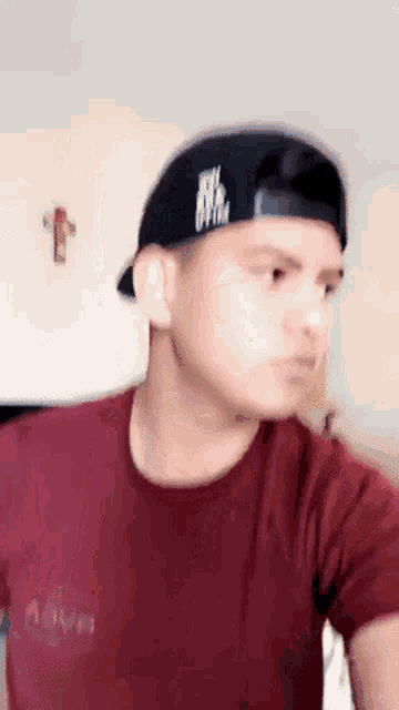 a young man wearing a red shirt and a black hat with a white logo on it