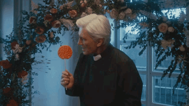 a priest is eating a lollipop in front of a flower arrangement