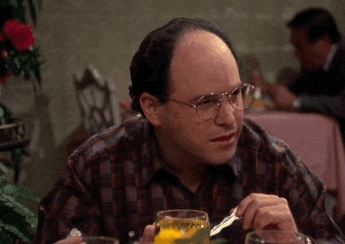 a bald man with glasses is sitting at a table with a glass of orange juice