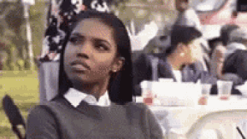 a woman is sitting at a table in front of a crowd and looking at the camera .