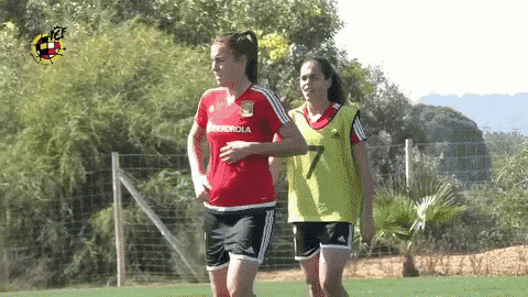 two female soccer players are running on a field and one has the number 7 on her vest