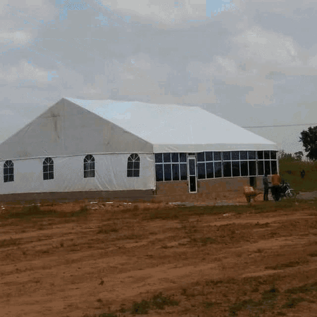 a large white tent with a lot of windows is sitting in the middle of a dirt field .