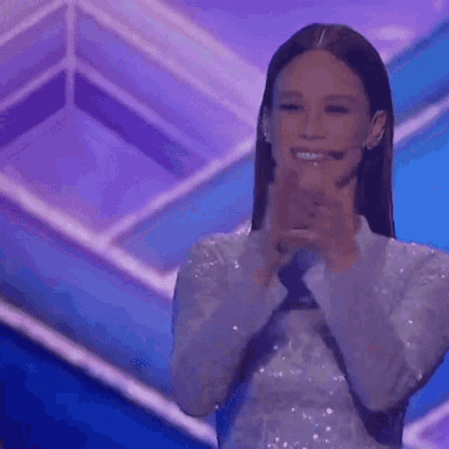 a woman in a white dress is applauding on a stage with the name mariana ximenez written on it .