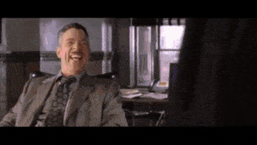 a man in a suit and tie is laughing while sitting in a chair .