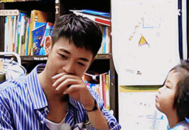 a man in a blue and white striped shirt is covering his mouth while talking to a little girl