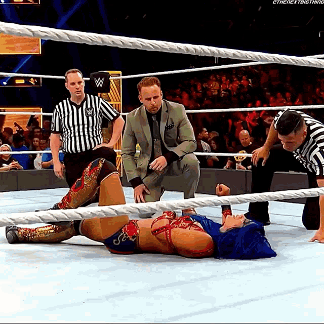 a woman is laying on the ground in a wrestling ring while a referee watches
