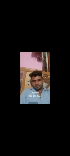 a man with a beard is sitting on a bed with a pink background .