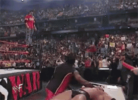a man in a red shirt is jumping in the air in front of a crowd with a sign that says wrestlemania on it