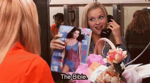 a woman is holding a magazine and talking on a phone while another woman looks at her .
