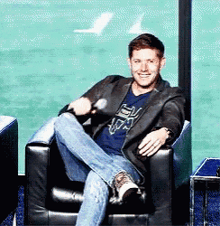 a man is sitting in a chair with his legs crossed and a microphone in his hand .