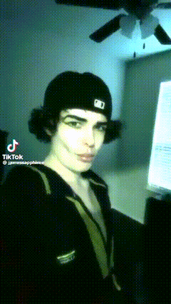 a young man wearing a black hat with the letter d on it is standing in front of a computer .