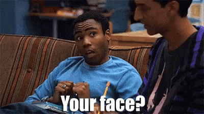 two men are sitting on a couch and one of them is saying your face